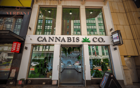 Street view of a modern cannabis dispensary with large glass windows, a “Cannabis Co.” sign above the entrance, and the Verdant Strategies logo in the corner.