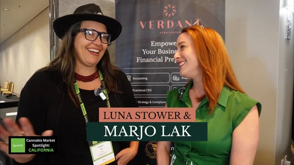 Luna Stower and Marjo Lak smile during an interview at the Verdant Strategies booth at the IgniteIt Cannabis Market Spotlight in California. A Verdant banner reading “Empowering Your Business with Financial Preparedness” is visible in the background.